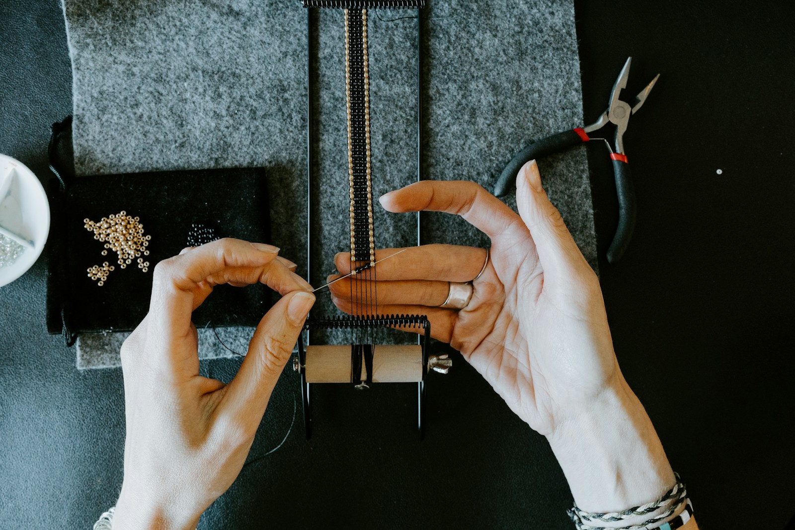 Jeweler weaving beads at a workbench with pliers and tools